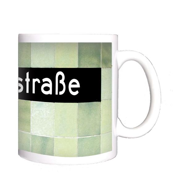 U-Bahnhof Voltastrasse Kaffeetasse - weiße Schrift auf schwarzem Schild, vor Mosaikwand in diversen Grüntönen