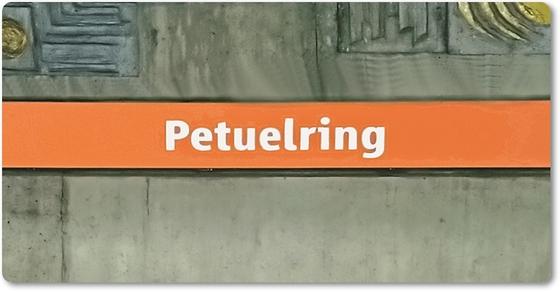 U-Bahnhof Petuelring Kühlschrankmagnet - weiße Schrift auf orangem Streifen, vor grauer Wand mit künstlerischen Elementen