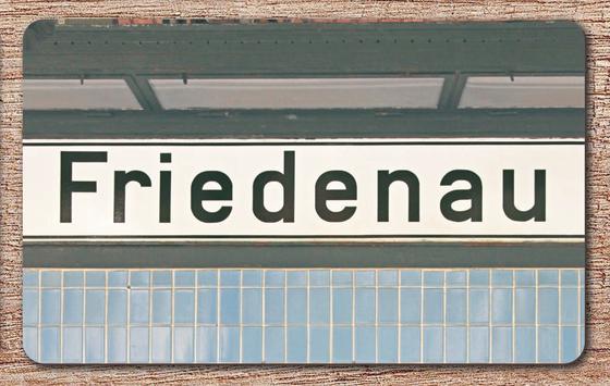 S-Bahnhof Friedenau S-Bahn Souvenir Frühstücksbrettchen  Berlin - weißes Schild mit schwarzer, schlichter Schrift, schwarz umrandet, über blauen Fliesen