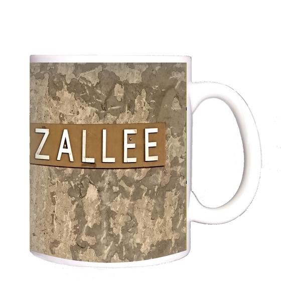 U-Bahnhof Lipschitzallee Kaffeetasse - weiße Schrift auf bronzefarbenem Schild, vor beige-braun geflecktem Hintergrund