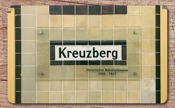 U-Bahnhof Kreuzberg - weißes Schild mit schwarzer Schrift und schwarzem Rand, unter Glasscheibe mit Inschrfit "Historischer Bahnhofsname 1926-1937"