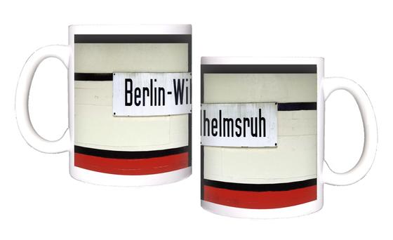 Kaffeebecher mit Aufdruck der originalgetreuen Gestaltung des Berliner S-Bahnhofs Wilhelmsruh rund um das Stationsschild - weiss gestrichene Ziegel mit balkenartigen schwarzen Verstrebungen, die ein weisses Emailleschild mit schwarzer Schrift einrahmen - 