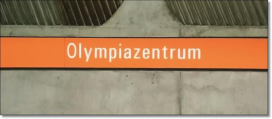 U-Bahnhof Olympiazentrum München Kaffeetasse - weiße Schrift auf orangem Schild vor grauer Betonwand