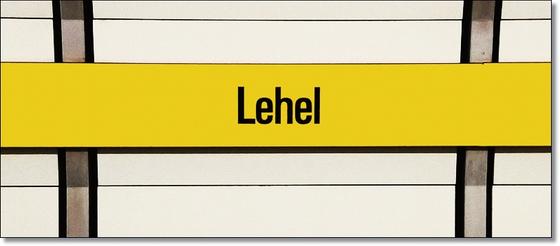 U-Bahnhof Lehel Kaffeetasse - schwarze Schrift auf gelbem Streifen, vor weißer Plattenwand