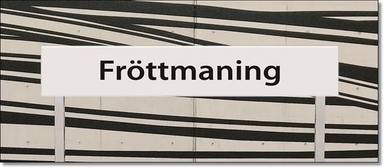 U-Bahnhof Fröttmaning Kaffeetasse - schwarze Schrift auf weißem Schild, vor weißem Hintergrund mit dynamischen, schwarzen Streifen
