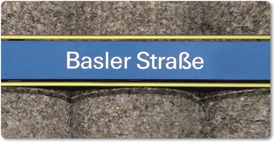 U-Bahnhof Basler Straße Kühlschrankmagnet - weiße Schrift auf hellblauem Schild, gelb umrandet, vor grauer Säulenwand