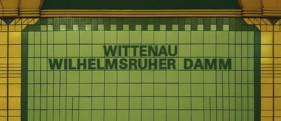 U-Bahn-Tasse Berlin Wittenau Wilhelmsruher Damm der Linie U8 in der originalgetreuen Stations-Gestaltung mit schwarzem Schriftzug auf olivgrünen Fliesen und in senfgelber Rahmung Ansicht Tasse links und rechts