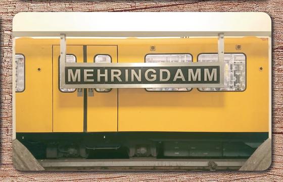 U-Bahnhof Mehringdamm Frühstücksbrettchen - weiße Schrift auf schwarzem Schild, vor gelber Ubahn