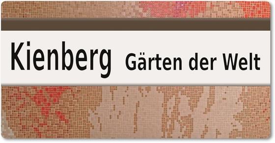 U-Bahnhof Kienberg - Gärten der Welt - schwarze Schrift auf weißem Schild im Hintergrund ein Abstraktes Design in lachs-rosa und beige