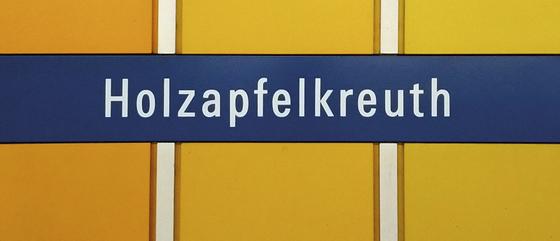 U-Bahn-Tasse mit dem Schriftzug des Muenchner Bahnhofs Holzapfelkreuth der Linie U6 - Dunkelblaues Schild mit weissem Text auf orangenem Grund  