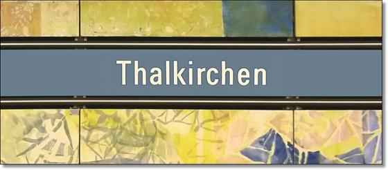 U-Bahnhof Thalkirchen Kaffeetasse - weiße Schrift auf blauem Schild, mit schwarzer Umrandung, auf abstraktem Muster in blau-gelb