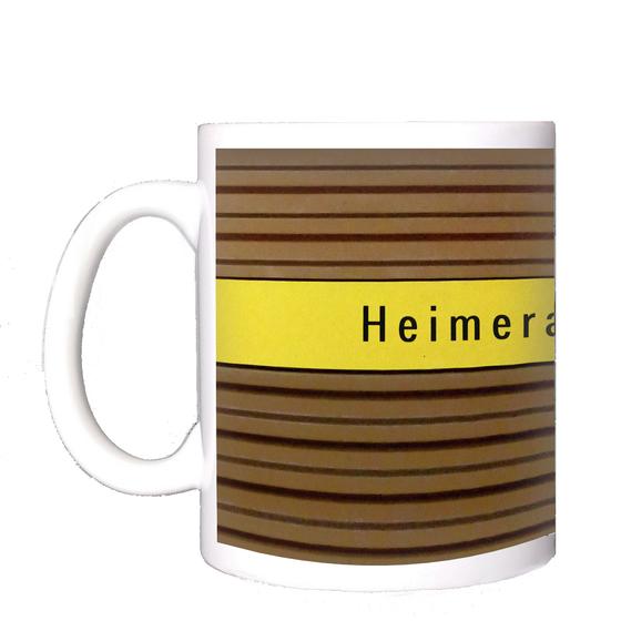 U-Bahnhof Heimeranplatz Kaffeetasse - schwarze Schrift auf gelbem Streifen, vor braunem Riffelhintergrund