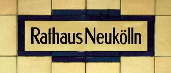U-Bahnhof Rathaus Neukölln Kaffeetasse - schwarze Schrift auf gelblich-beigem Schild, umrandet von dunkelblauen Fliesen, welche wiederum von beigen Fliesen begrenzt werden
