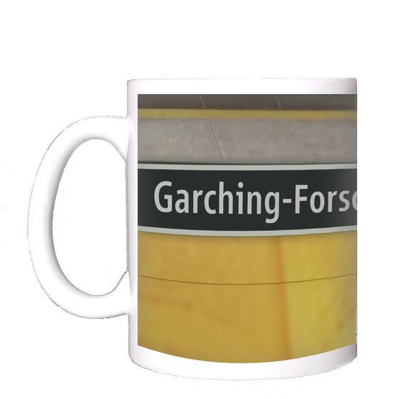 U-Bahnhof Garching-Forschungszentrum Kaffeetasse - weiße Schrift auf schwarzem Schild, zwischen gelblicher Plattenwand mit Buchseiten-Print und grauen Platten