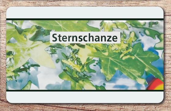 U-Bahnof Hamburg Frühstücksbrettchen - schwarze Schrift auf weißem Schild vor abstraktem, grünem Blättermuster 