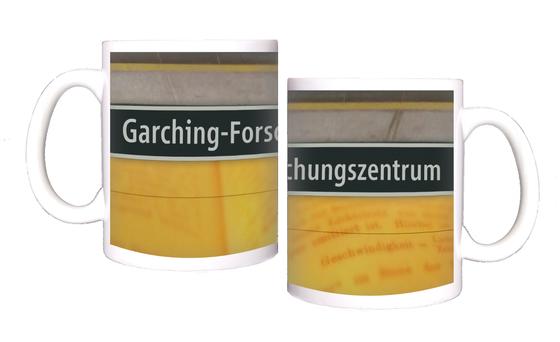 U-Bahnhof Garching-Forschungszentrum Kaffeetasse - weiße Schrift auf schwarzem Schild, zwischen gelblicher Plattenwand mit Buchseiten-Print und grauen Platten
