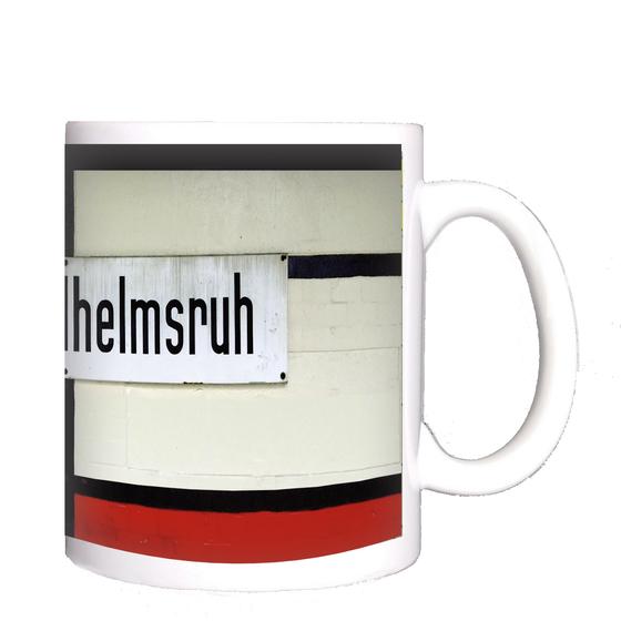 Kaffeebecher mit Aufdruck der originalgetreuen Gestaltung des Berliner S-Bahnhofs Wilhelmsruh rund um das Stationsschild - weiss gestrichene Ziegel mit balkenartigen schwarzen Verstrebungen, die ein weisses Emailleschild mit schwarzer Schrift einrahmen - 