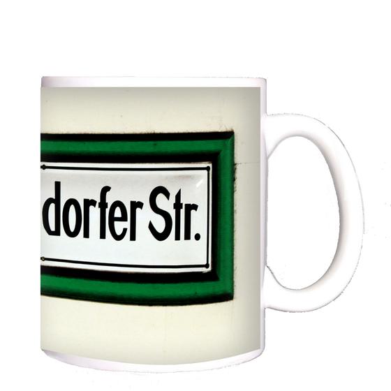 U-Bahnhof Reinickendorfer Straße Kaffeetasse - schwarze Schrift auf weißem Schild, mit dickem, grünem Rahmen, vor weißer Wand