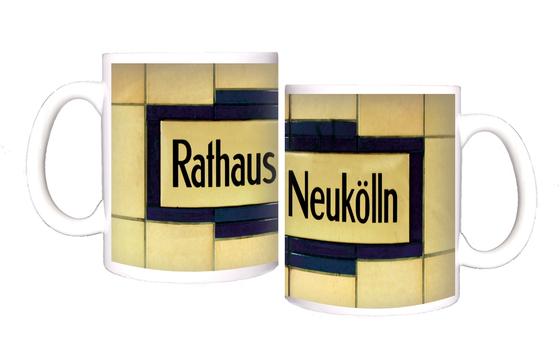 U-Bahnhof Rathaus Neukölln Kaffeetasse - schwarze Schrift auf gelblich-beigem Schild, umrandet von dunkelblauen Fliesen, welche wiederum von beigen Fliesen begrenzt werden
