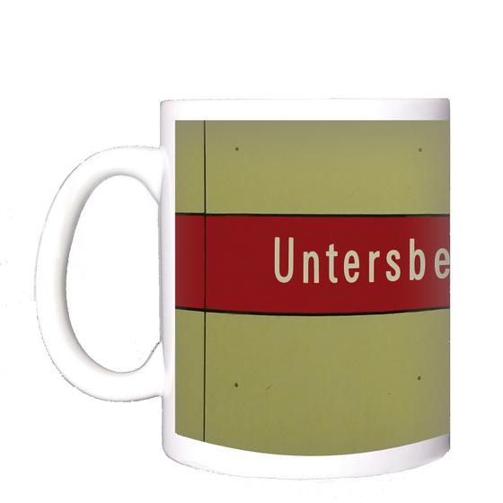 U-Bahnhof Untersbergstraße Kaffeetasse - weiße Schrift auf rotem Streifen, vor beiger Plattenwand