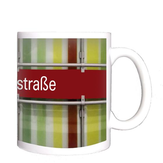 U-Bahnhof Dülferstraße Kaffeetasse - weiße Schrift auf rotem Schild auf Metallgestell, vor Streifenhintergrund in diversen Grüntönen