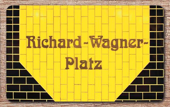 U-Bahnhof Richard-Wagner-Platz U-Bahn Souvenir Frühstücksbrettchen - braune, verschlungene Schrift auf gelbem Kachelhintergrund, umrandet von schwarzen Kacheln