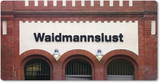 S-Bahnhof Waidmannslust - schwarze Lettern auf heller Hauswand außerdem Torbögen und Details in Backsteinoptik