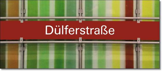 U-Bahnhof Dülferstraße Kaffeetasse - weiße Schrift auf rotem Schild auf Metallgestell, vor Streifenhintergrund in diversen Grüntönen