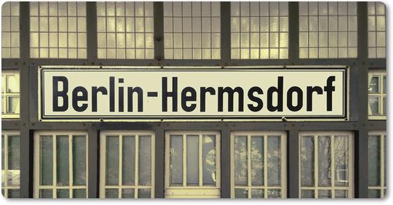 S-Bahnhof Berlin Hermsdorf - schwarze Schrift aus weißem Schild auf Fassade voller Fenster