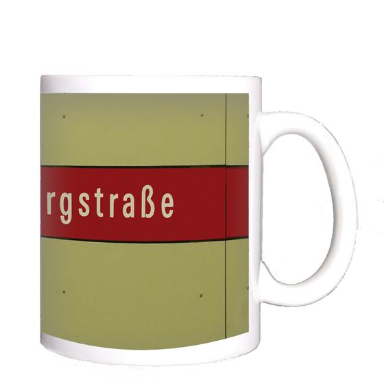 U-Bahnhof Untersbergstraße Kaffeetasse - weiße Schrift auf rotem Streifen, vor beiger Plattenwand