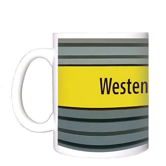 U-Bahnhof Westendstraße Kaffeetasse - schwarzer Schrift auf gelbem Schild, vor grau-blauer Wand mit schwarzen Streifen