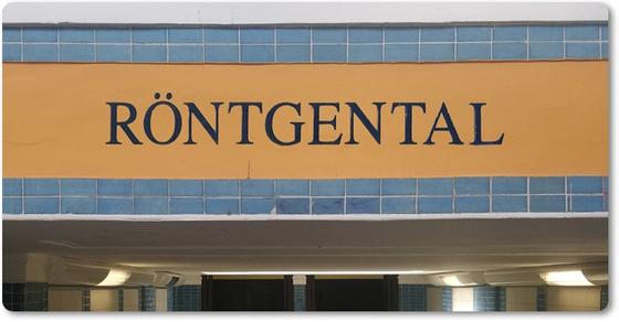 S-Bahn-Kühlschrankmagnet Röntgental schwarze Schrift auf orangenem Hintergrund über türkisen Kacheln darunter der Eingang zur Station