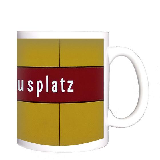 U-Bahnhof Kolumbusplatz Kaffeetasse - weiße Schrift auf dunkelrotem Streifen, vor gelber Plattenwand