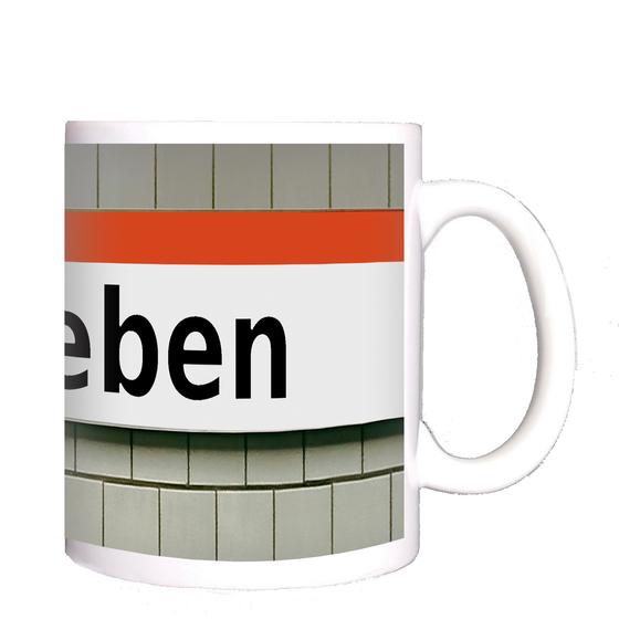 U-Bahnhof Ruhleben Kaffeetasse - schwarze Schrift auf weißem Schild mit orangem Streifen auf weißer Fliesenwand