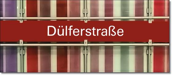 U-Bahnhof Dülferstraße Kaffeetasse - weiße Schrift auf rotem Schild auf Metallgestell, vor Streifenhintergrund in diversen Rottönen