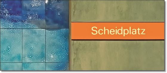 U-Bahnhof Scheidplatz Kaffeetasse - weiße Schrift auf orangem Streifen, vor braun-beiger Wand mit blauen Fliesen am linken Rand