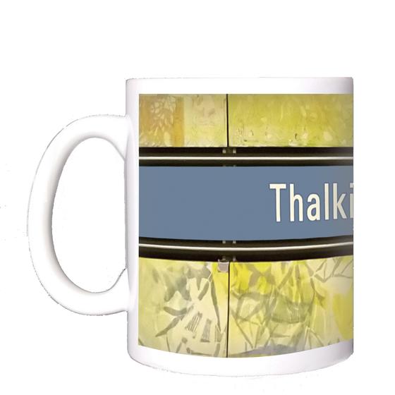 U-Bahnhof Thalkirchen Kaffeetasse - weiße Schrift auf blauem Schild, mit schwarzer Umrandung, auf abstraktem Muster in blau-gelb