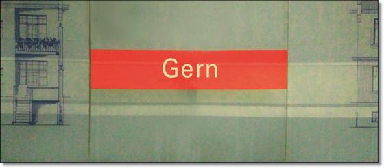 U-Bahnhof Gern Kaffeetasse - weiße Schrift auf rotem Schild, vor grauer Steinwand, mit blauer Zeichnung auf der linken Seite