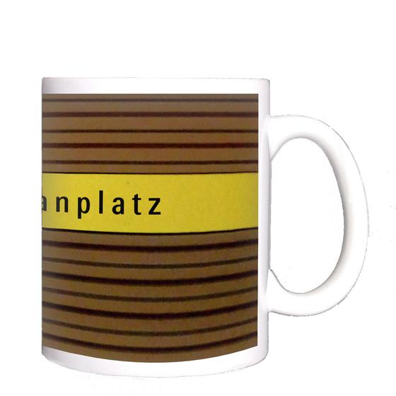 U-Bahnhof Heimeranplatz Kaffeetasse - schwarze Schrift auf gelbem Streifen, vor braunem Riffelhintergrund