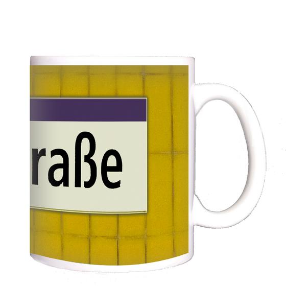 U-Bahnhof Seestraße Kaffeetasse - schwarze Schrift auf weißem Schild mit lila Streifen, vor gelber Mosaikwand