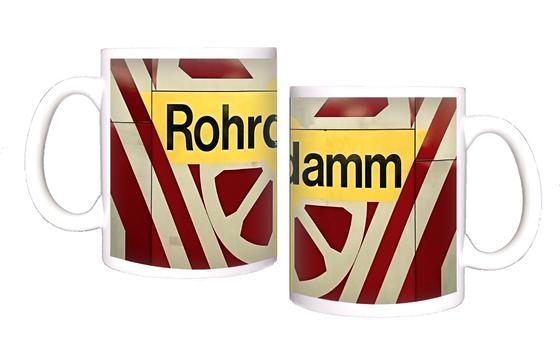 U-Bahn-Kaffeetasse Berlin Rohrdamm - schwarze Schrift auf gelbem Schild, umrandet von weißem, radähnlichem Muster auf rot-braunem Untergrund