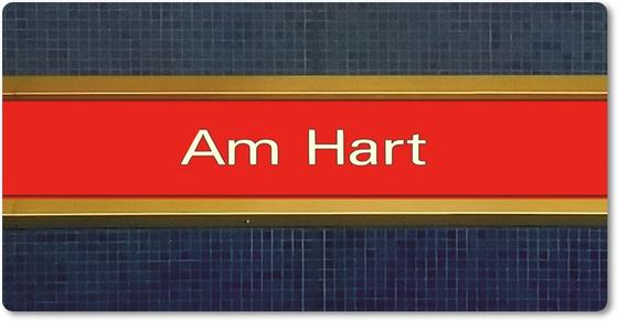 U-Bahnhof Am Hart - weiße Schrift auf rotem Streifen, mit goldener Umrandung vor blauem Moaik-Fliesenhintergrund