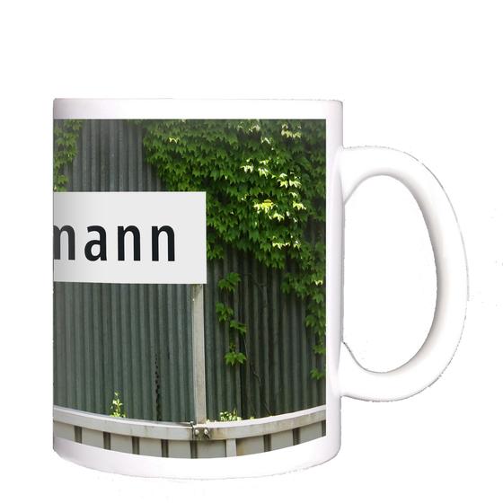 U-Bahnhof Freimann Kaffeetasse - schwarze Schrift auf weißem Schild vor grauem Wellblech mit Rankpflanze