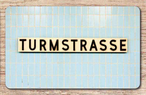 U-Bahnhof Turmstrasse Frühstücksbrettchen - weißes Schild mit schwarzer, schlichter Schrift auf blauen Fliesen