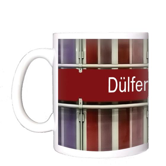 U-Bahnhof Dülferstraße Kaffeetasse - weiße Schrift auf rotem Schild auf Metallgestell, vor Streifenhintergrund in diversen Rottönen