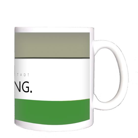 U-Bahnhof Garching Kaffeetasse - Garching Wappen mit schwarzer Schrift auf weißem Streifen, über grünem Streifen, unter beige-gelbem Streifen