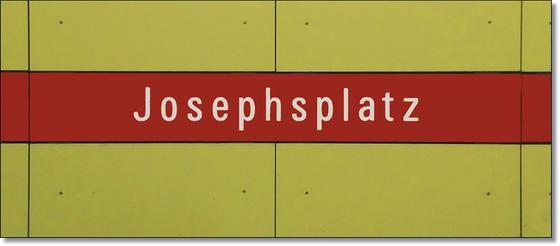 U-Bahn Tasse Josephsplatz - weiße Schrift auf rotem Streifen, vor gelber Wand