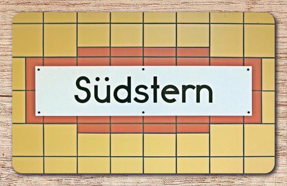 U-Bahnhof Südstern Frühstücksbrettchen - weißes Schild mit schwarzer, schlichter Schrift auf weißem Schild mit rötlich-brauner Umrandung auf orange-gelben Fliesen