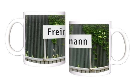 U-Bahnhof Freimann Kaffeetasse - schwarze Schrift auf weißem Schild vor grauem Wellblech mit Rankpflanze