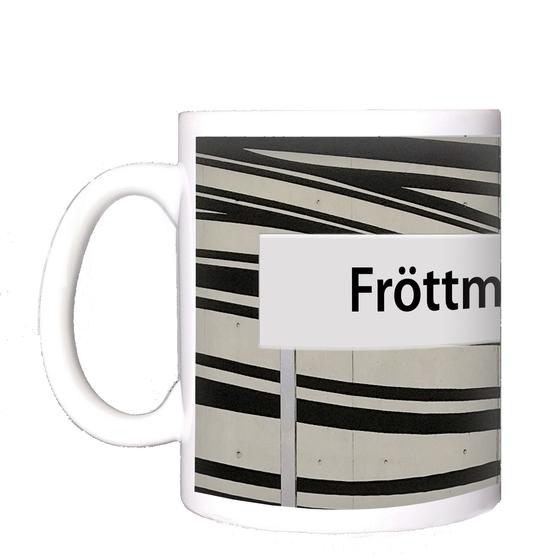 U-Bahnhof Fröttmaning Kaffeetasse - schwarze Schrift auf weißem Schild, vor weißem Hintergrund mit dynamischen, schwarzen Streifen